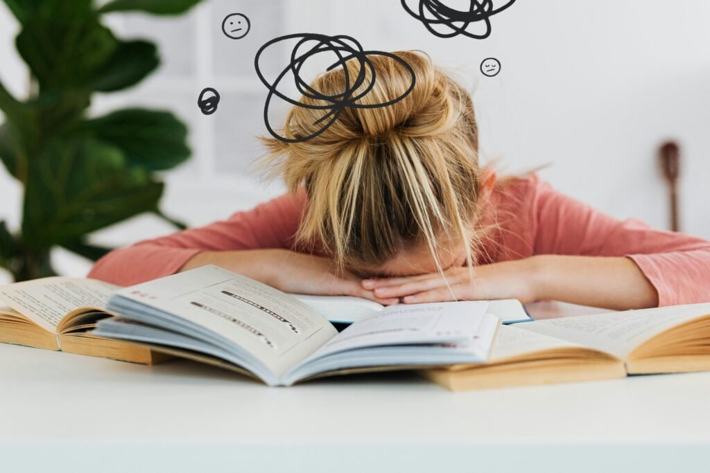 Girl with her head resting on a pile of open books, with drawn squiggles representing stress above her head.