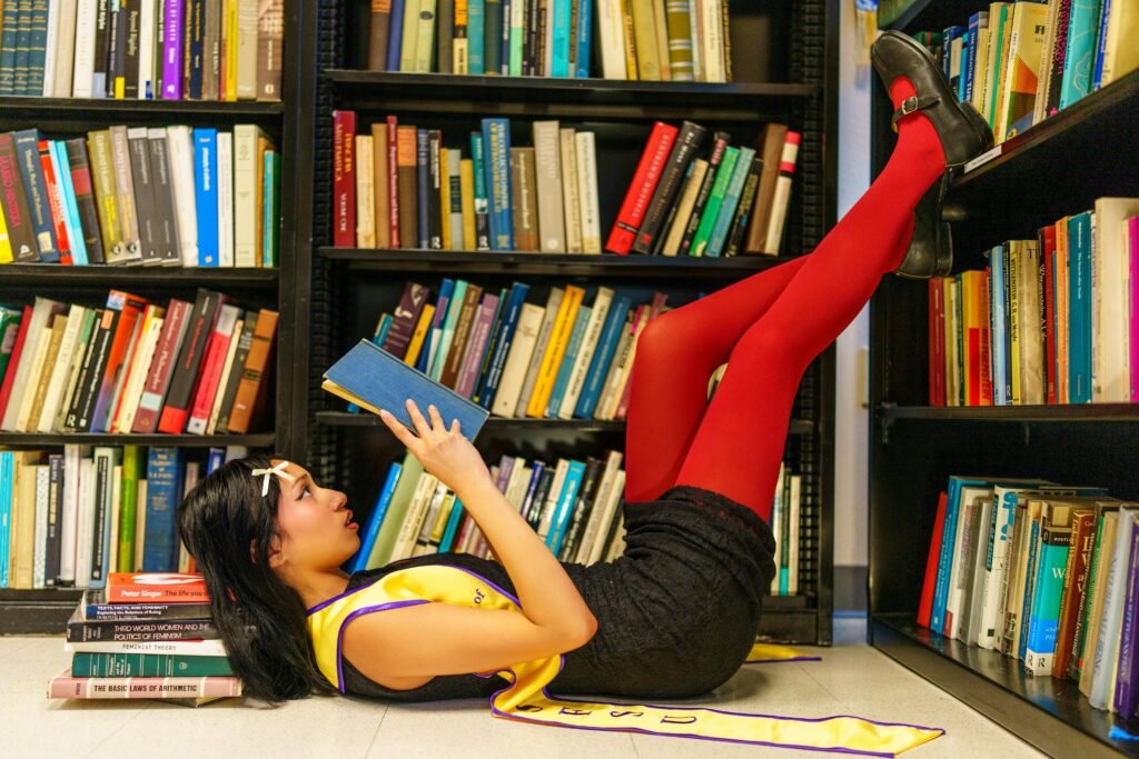 Young woman reading a book while lying down in a library surrounded by colorful books.