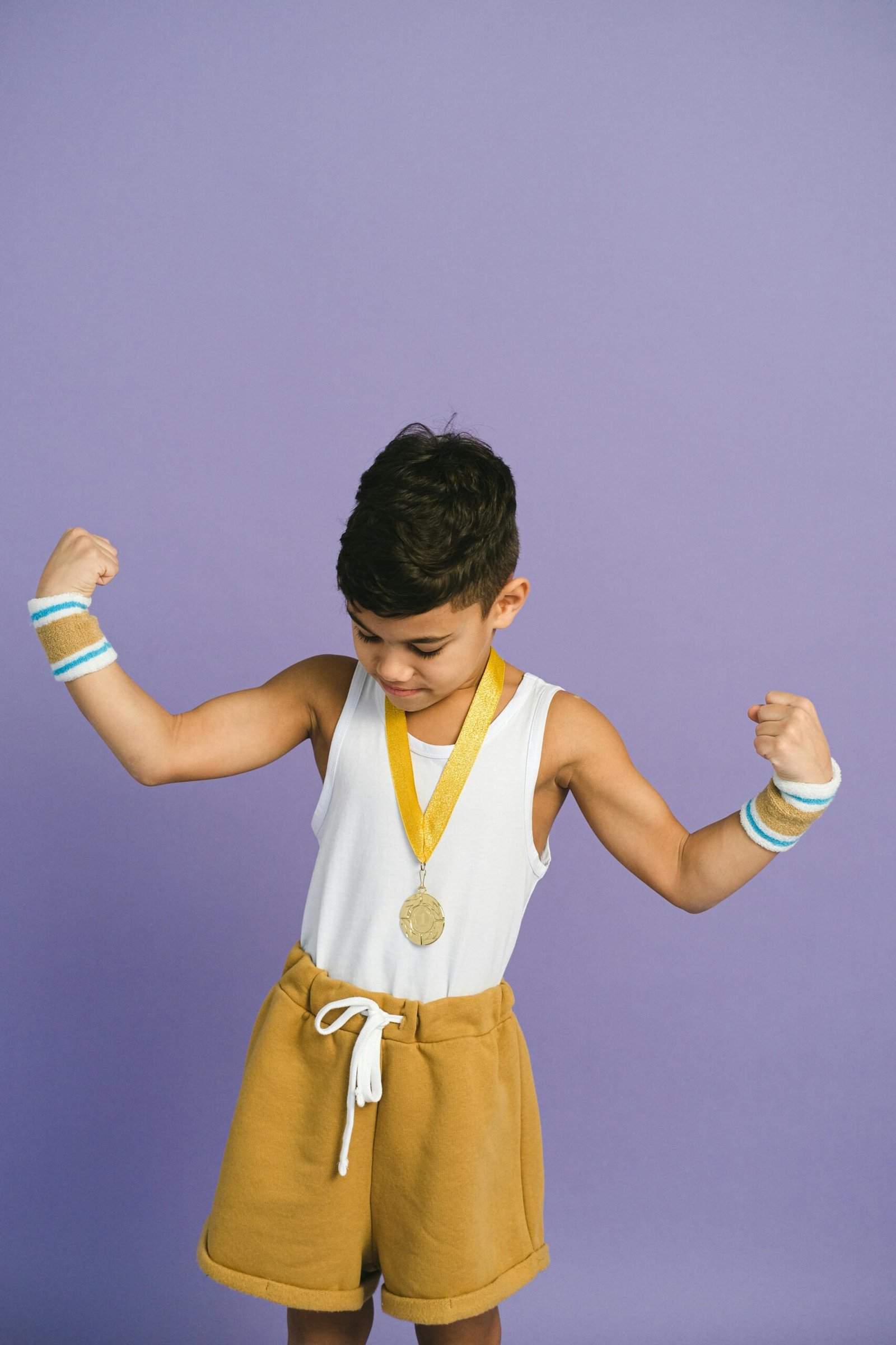 Young boy flexing his arms while wearing a medal against a purple background