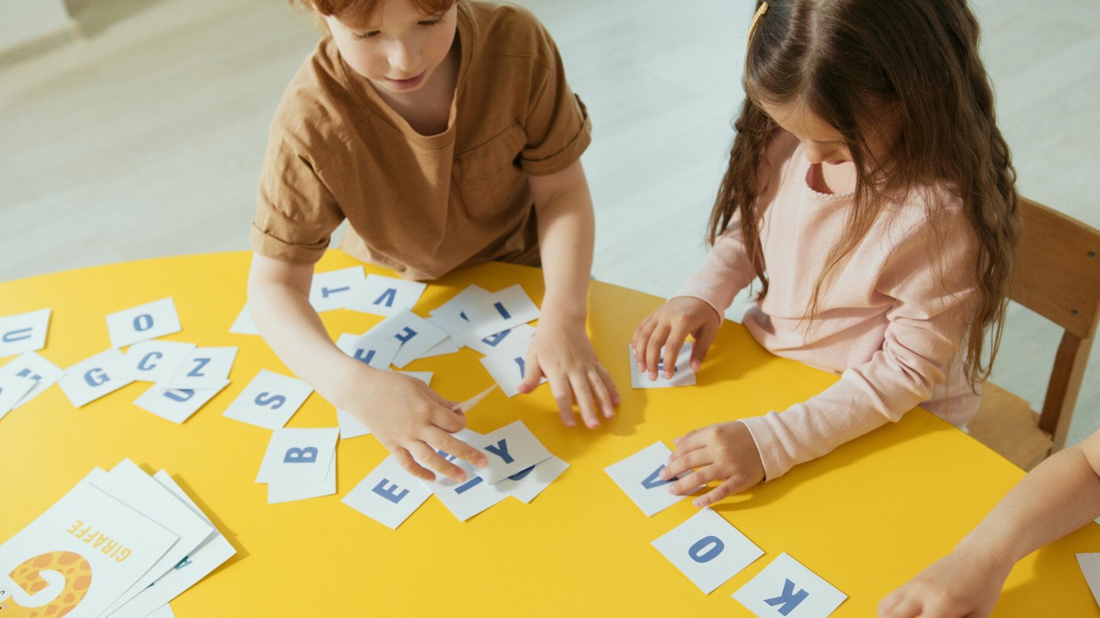 Two children arranging alphabet cards on a yellow table